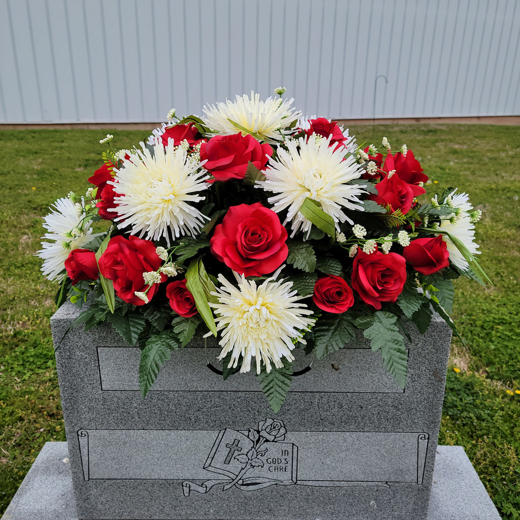 A headstone saddle with red roses and cream mum grave flowers for cemetery, funeral, and memorial decorations.