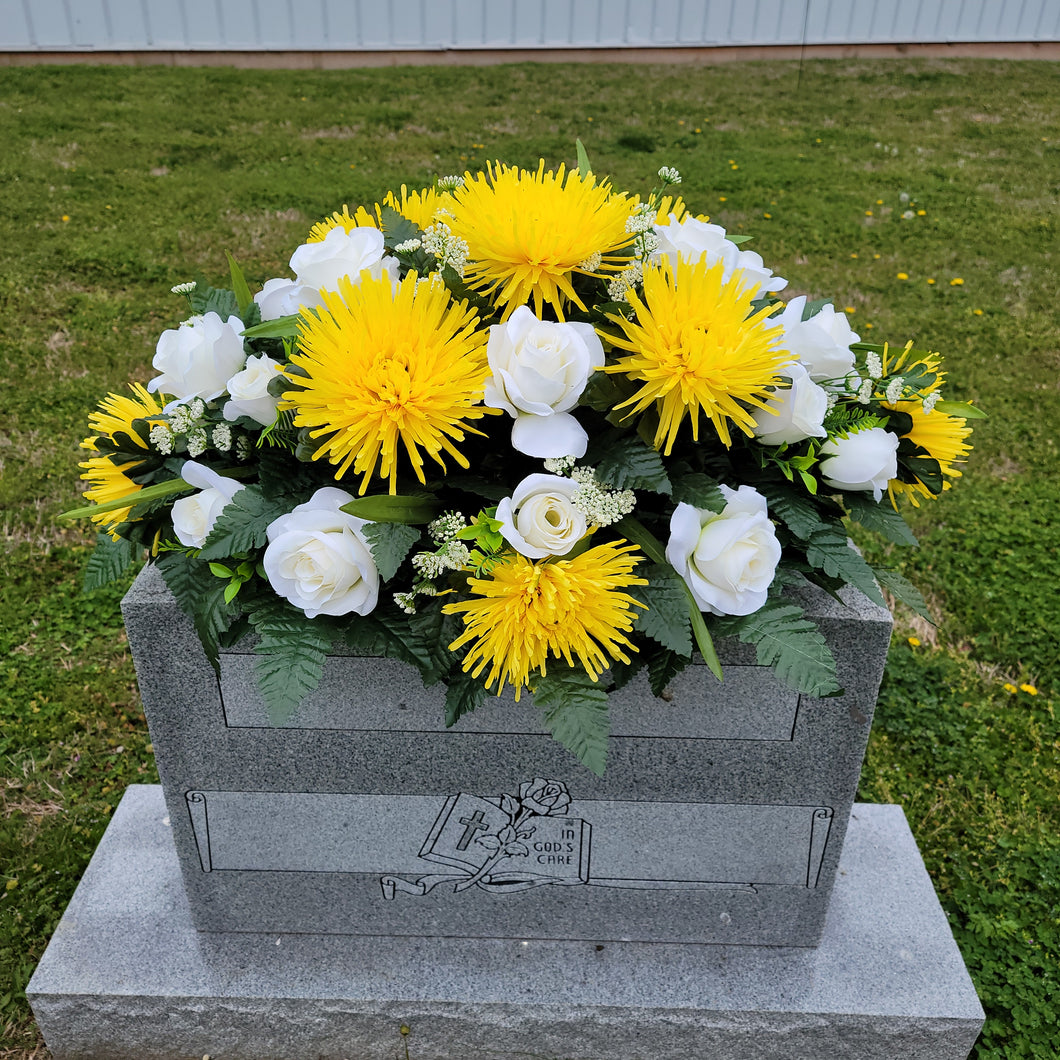 A headstone saddle with cream roses and yellow mum grave flowers for cemetery, funeral, and memorial decorations.