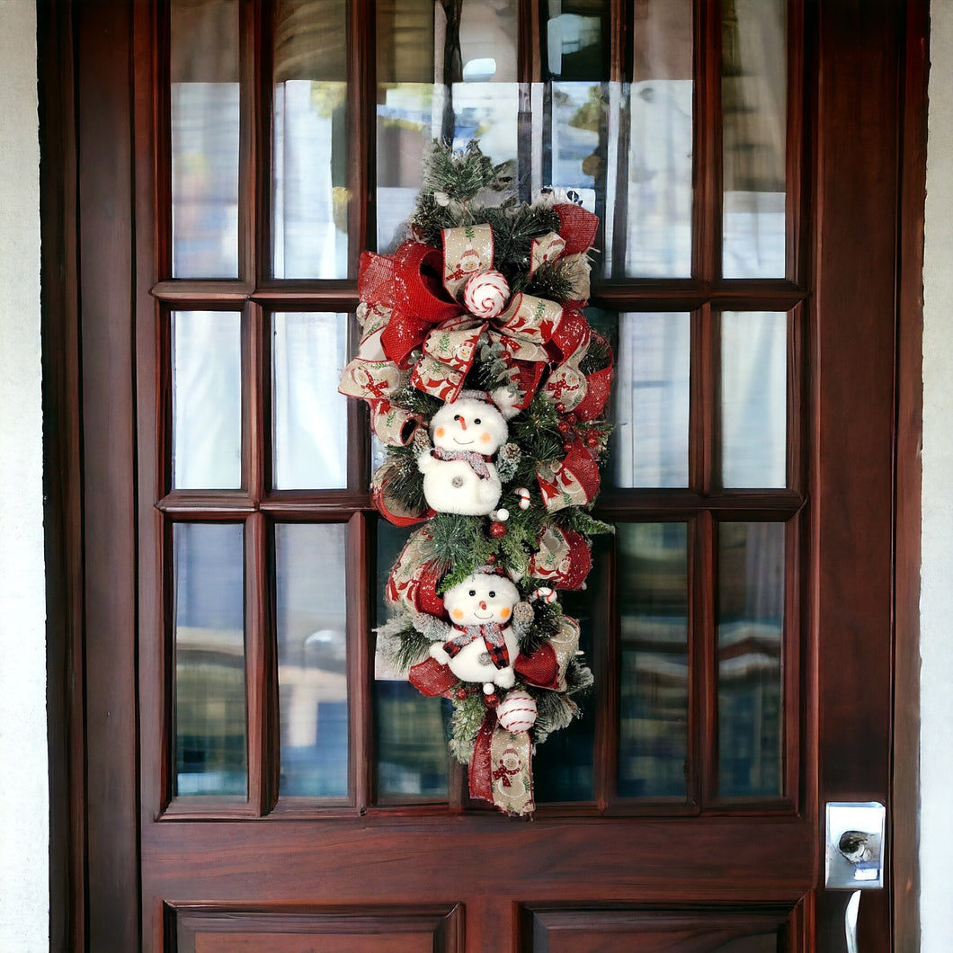 This teardrop door hanging wreath is a festive swag for the Christmas season. It has 2 snowmen, pine, berries, and 2 types of ribbon.