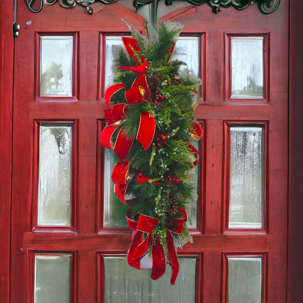 This is a teardrop door hanger festive swag for Christmas season. It has red & blue berries, pinecones, cardinals, and red velvet ribbon.