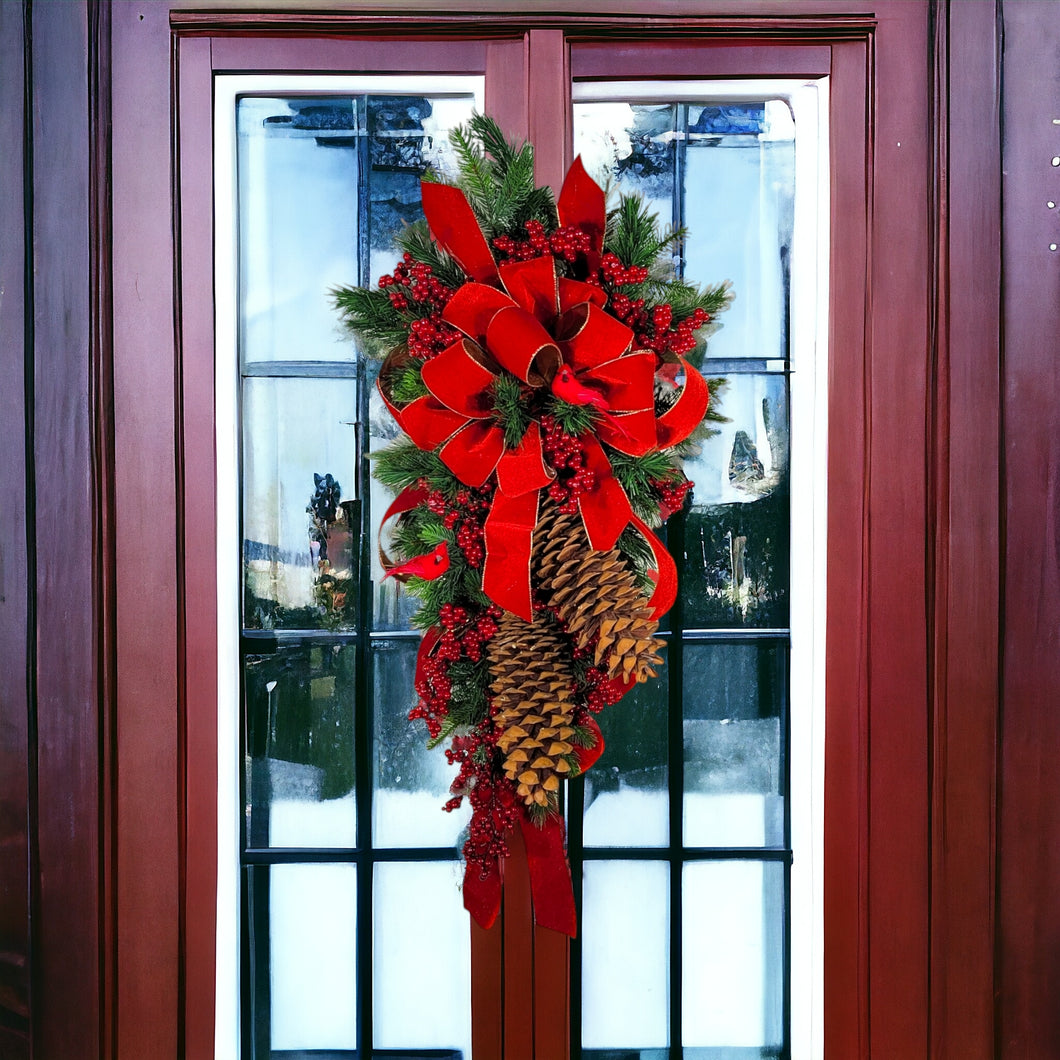 This is a teardrop door hanging that is festive for the Christmas season. It has pinecones, berries, pine, and a cardinal.