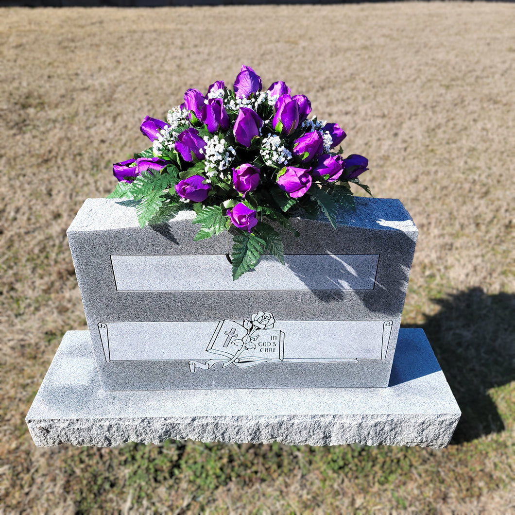 Headstone saddle with purple rosebud grave flowers. It is a funeral, cemetery, or memorial decoration.