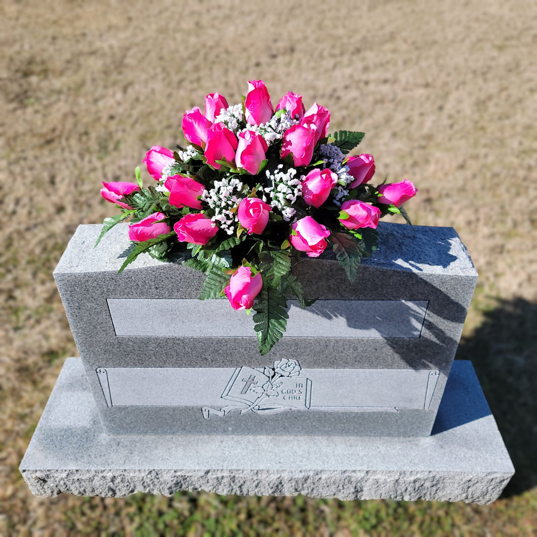 Headstone saddle with pink rosebud grave flowers. It is a funeral, cemetery, or memorial decoration.