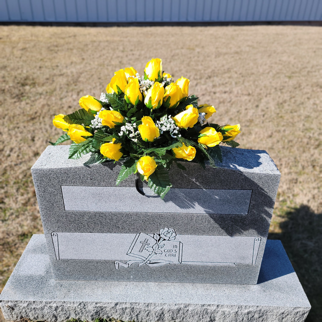 Headstone saddle with yellow rosebud grave flowers. It is a funeral, cemetery, or memorial decoration.