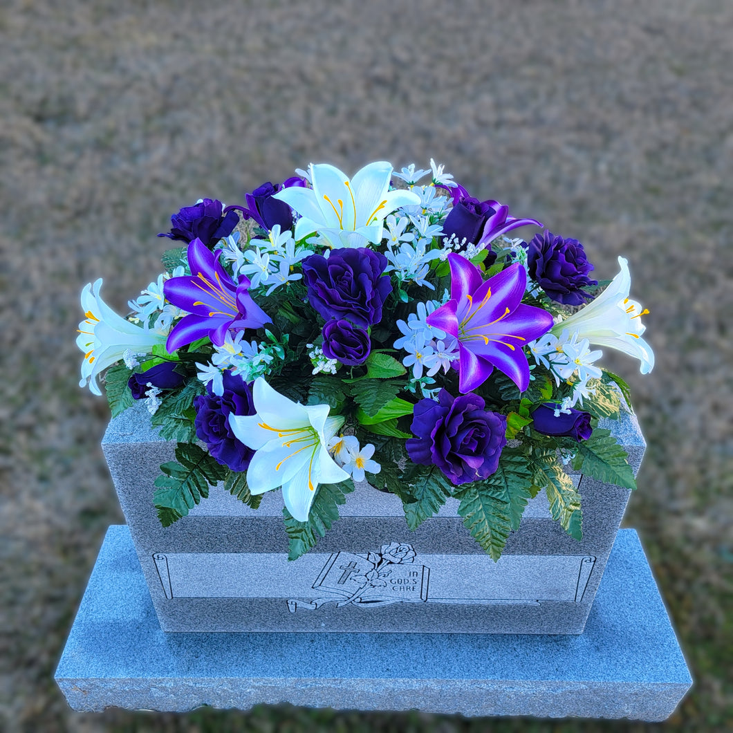 Headstone Saddle with purple & white trumpet lilies and purple roses. It is a grave flower cemetery, funeral, or memorial decoration.