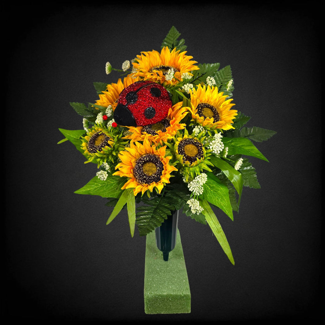 A cemetery cone with grave flowers including yellow sunflowers and a ladybug. This is a memorial decoration or flowers for funeral.